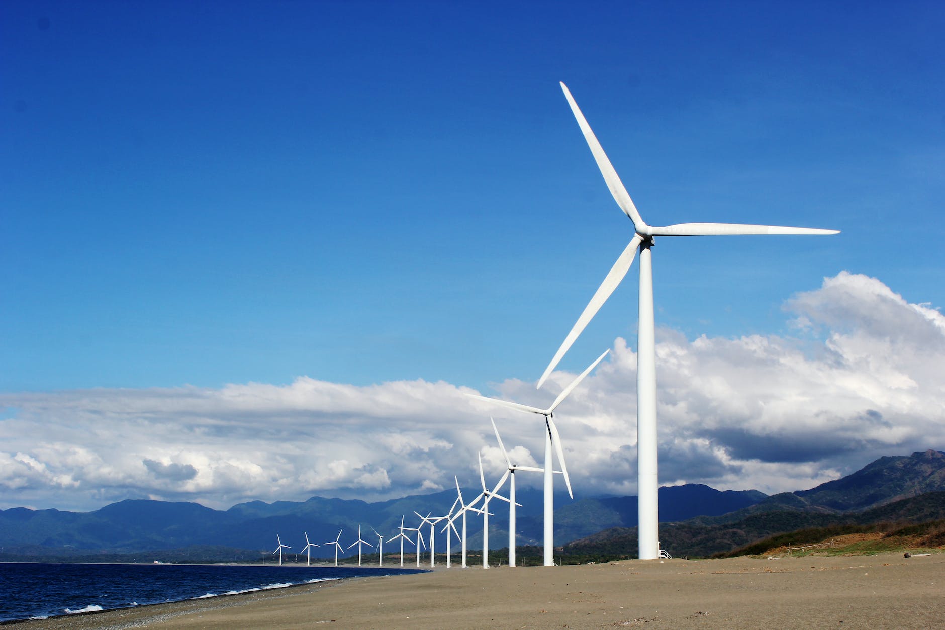 white wind turbines on gray sand near body of water