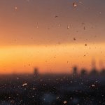 Tiny microplastic particles suspended in hazy urban air at dusk, glinting in warm amber light above a city skyline