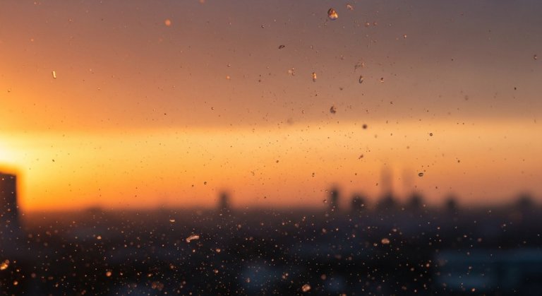 Tiny microplastic particles suspended in hazy urban air at dusk, glinting in warm amber light above a city skyline