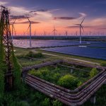 Aerial view of vast solar farm and wind turbines at sunset with abandoned oil infrastructure reclaimed by nature in the foreg
