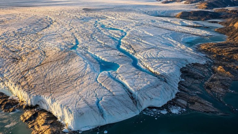 Aerial view of Greenland ice sheet with meltwater rivers and exposed rocky edges showing ice retreat